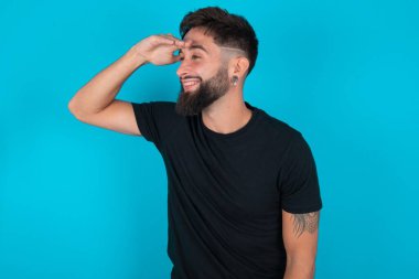 Siyah tişört giyen İspanyol sakallı adam mavi arka planda mutlu ve gülümsüyor. Konsept aranıyor.