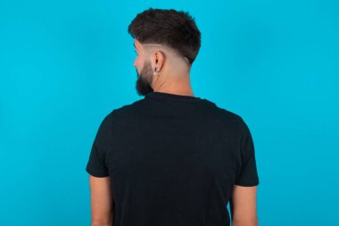 Mavi arka planda duran siyah tişört giyen İspanyol sakallı bir adamın arka yüzü. Stüdyo Çekimi.