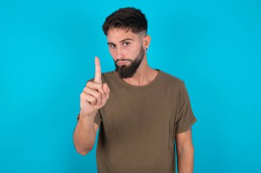 Genç İspanyol sakallı adam mavi arka planda duruyor hayal kırıklığına uğramış ve ön tarafı işaret ediyor.