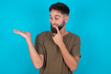 Pozitif, genç, İspanyol sakallı bir adam mavi arka plan reklamının karşısında duruyor.