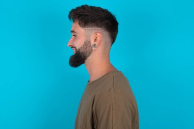 Mavi arka planda duran hoş, genç, İspanyol sakallı bir adamın profil portresi boş dişli bir gülümsemeye bak.