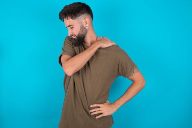 Mavi arka planda duran İspanyol sakallı genç adamın sırtı ağrıyordu.