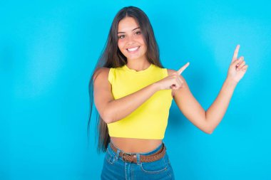 Mavi arkaplanda sarı kolsuz bluz giyen, iki parmağıyla ışıldayan ve boş fotokopi alanına bakan güzel bir kadın. Reklam kavramı.