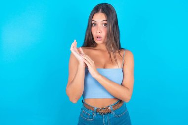 Mavi kolsuz bluz giyen duygusal esmer kadın avuçlarını ovuşturuyor ve inançsızlıkla kameraya bakıyor.