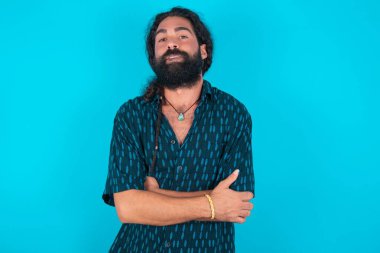 Sakallı, mavi gömlekli, beyaz bir adam. Ağzını ısırıyor. Endişeli ve korkmuş görünüyor..