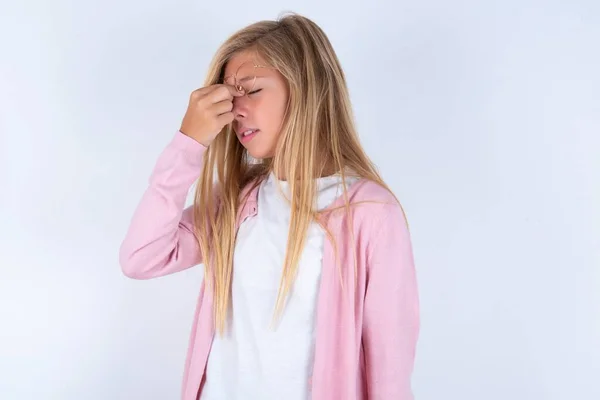 彼女の顔に手を握っている頭痛に苦しむ白い背景の上にピンクのジャケットとメガネを着ているブロンドの少女 — ストック写真