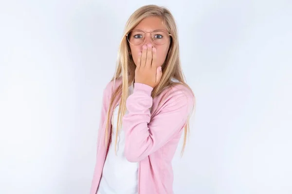 Маленькая Блондинка Розовой Куртке Очках Белом Фоне Покрывая Рот Рукой — стоковое фото