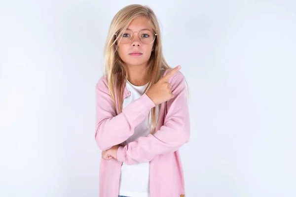 Blond Meisje Draagt Roze Jasje Bril Witte Achtergrond Wijzend Naar — Stockfoto