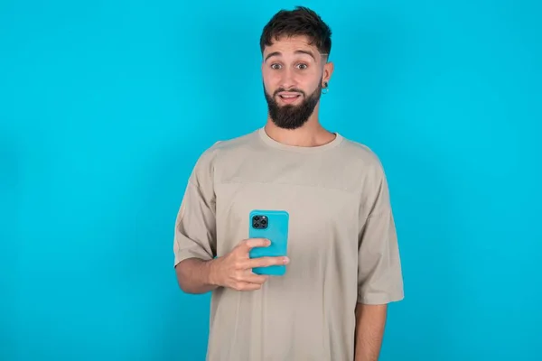 Vousatý Běloch Neformálním Tričku Přes Modré Pozadí Drží Mobilní Telefon — Stock fotografie