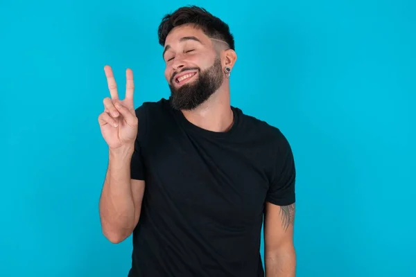 Mladý Hispánský Vousatý Muž Černém Tričku Stojící Modrém Pozadí Usmívající — Stock fotografie