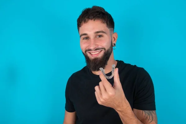 Jovem Hispânico Barbudo Vestindo Camiseta Preta Contra Fundo Azul Segurando — Fotografia de Stock