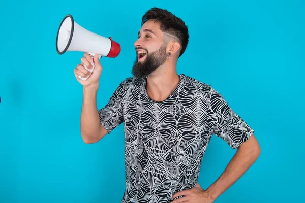Mavi arka planda duran komik, genç, İspanyol sakallı adam samimi duygular ve yaşam tarzı kavramı. Kopyalama alanı oluşturun. Megafonla bağırıyordu..