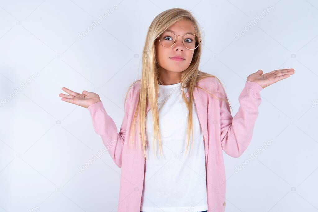 Blonde little girl wearing pink jacket and glasses over white background with arms out, shrugging shoulders, saying: who cares, so what, I don't know.