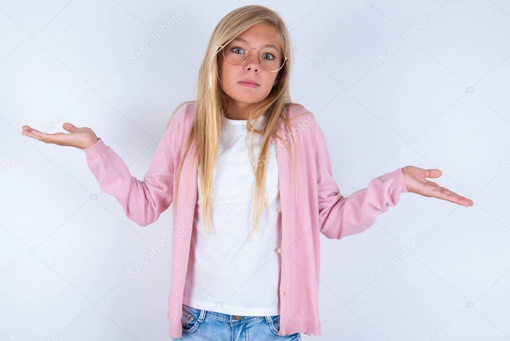 Blonde little girl wearing pink jacket and glasses over white background shrugging her shoulders, saying: who cares, so what, I don't know.