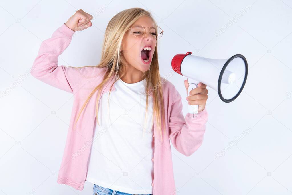 Blonde little girl wearing pink jacket and glasses over white background communicates shouting loud holding a megaphone