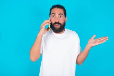 Mavi arka planda beyaz tişörtlü beyaz sakallı beyaz bir adam telefonda konuşurken yüz yüze, utanç ve şaşkınlıktan şok olmuş, sinirli ve hayal kırıklığına uğramış. Hata için korku ve üzüntü.