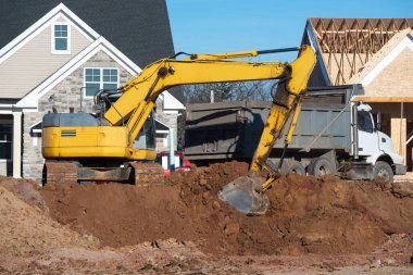 Kazıcı çakılları sarı bir kürekle kamyona yüklüyor.