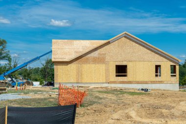 New residential frame house under construction against a blue sky plywood rof wall window