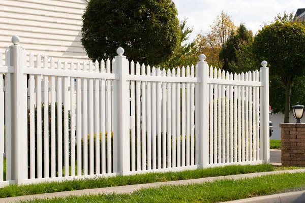 A new white vinyl fence by a grass area with trees behind it green property modern