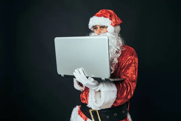 穿得像圣诞老人的男人拿着笔记本电脑发邮件 背景是黑色的 圣诞观念 圣诞老人 庆祝活动 — 图库照片