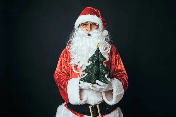 一个人穿着圣诞老人的衣服 拿着一棵布圣诞树 背景是黑色的 圣诞观念 圣诞老人 庆祝活动 — 图库照片