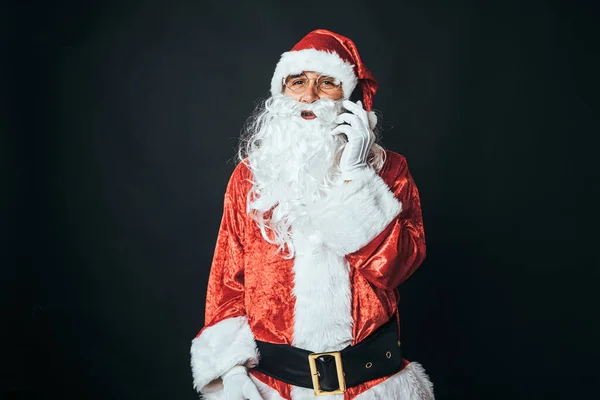 穿得像圣诞老人的男人在手机上说话 拿着一个黑色背景的自拍 圣诞观念 圣诞老人 庆祝活动 — 图库照片