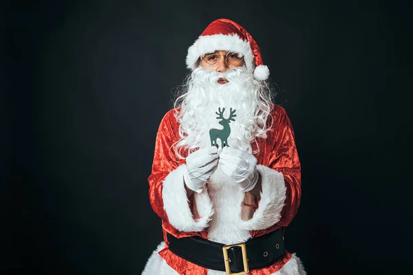 Człowiek Ubrany Jak Święty Mikołaj Trzymający Drewnianą Figurę Renifera Czarnym — Zdjęcie stockowe