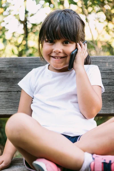 Mała Czarnowłosa Dziewczynka Ubrana Biały Shirt Siedząca Ławce Parku Rozmawiająca — Zdjęcie stockowe