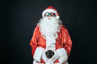 Noel Baba gibi giyinmiş, gözlüklü, televizyon ayarlı, siyah arka planda bir adam. Noel konsepti, Noel Baba, hediyeler, kutlamalar.