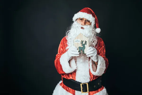 一个人穿着圣诞老人的衣服 拿着一只绿色的木制驯鹿 背景是黑色的 圣诞老人 庆典的概念 — 图库照片