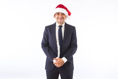 Takım elbiseli, kravatlı ve Noel Baba şapkalı beyaz arka planda gülümseyen bir iş adamı. Noel kutlaması kavramı.