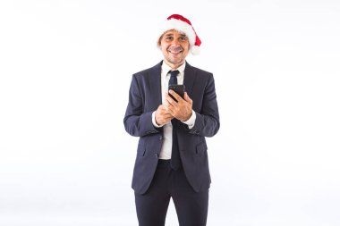Takım elbiseli, kravatlı ve Noel Baba şapkalı, gülümseyen, telefonu tutan beyaz arka planda bir iş adamı. Noel kutlaması kavramı.