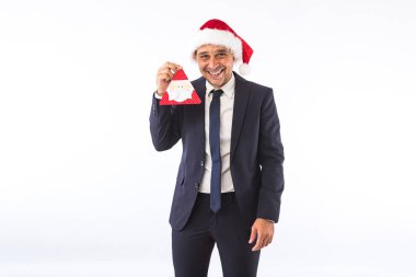 Takım elbiseli, kravatlı, Noel Baba şapkalı, gülümseyen, elinde Noel Baba süsü tutan bir iş adamı. Noel kutlaması kavramı.