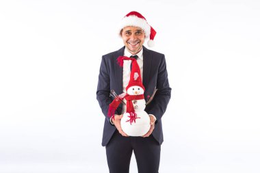 Takım elbiseli, kravatlı ve Noel Baba şapkalı beyaz arka planda bir kardan adamla gülümseyen bir iş adamı. Noel kutlaması kavramı.