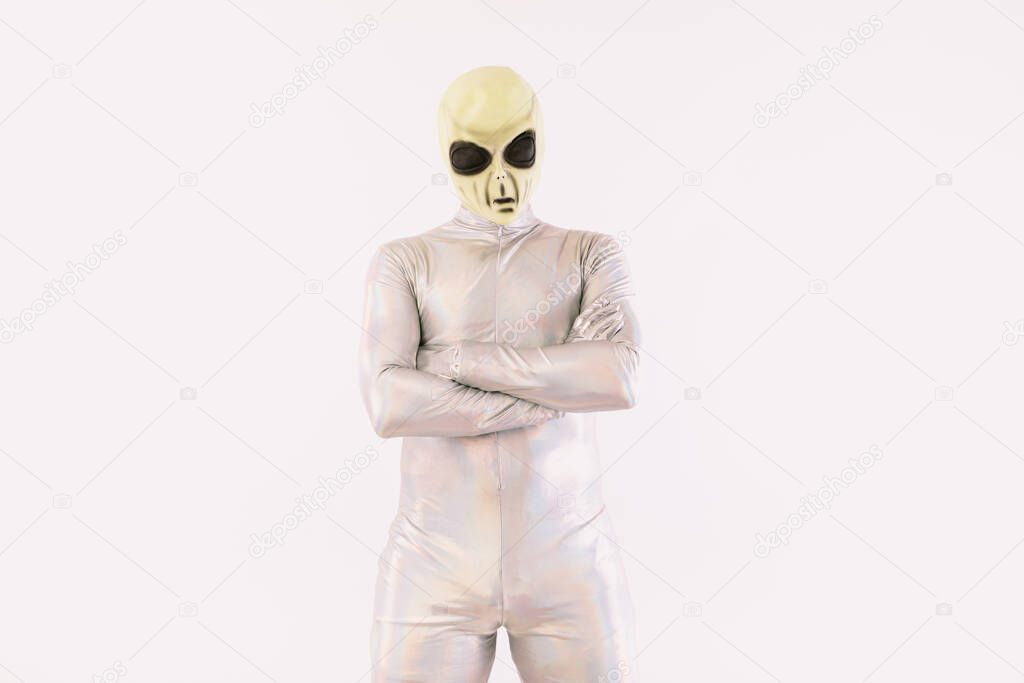 Person dressed in silver suit and green alien mask with crossed arms, on white background