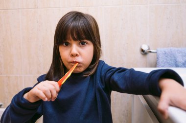 Dişlerini fırçalayan koyu mavi kazaklı küçük kız banyoda. Diş fırçalama, hijyen ve çocukluk konsepti.