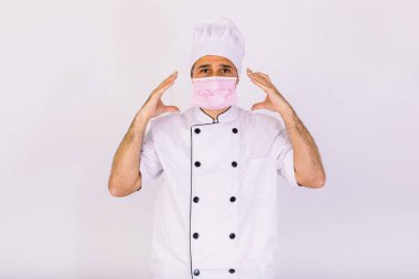 Aşçı mutfak ceketi ve şapkası giyiyor, pembe bir maske takıyor, beyaz arka planda.