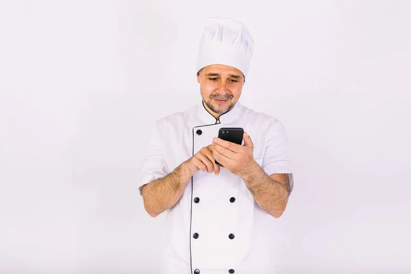 Kucharz Ubrany Biały Kapelusz Kurtkę Patrząc Jego Telefon Komórkowy Białym — Zdjęcie stockowe