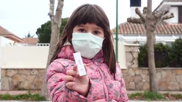 Little Girl Street Wearing White Mask Holding Teaching Negative Antigen — Stockvideo