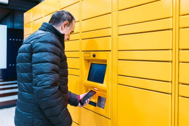 Ceketli adam sarı dolaptan bir paket almak için cep telefonundaki kodu tarıyor. Mesajlaşma kavramı, çevrimiçi, e-ticaret ve paketleri karşılaştırın