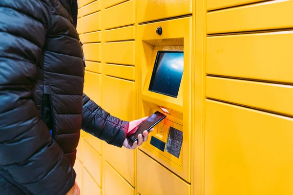 Sarı dolaptan bir paket almak için cep telefonundaki kodu tarayan bir adamın kolu. Mesajlaşma kavramı, çevrimiçi, e-ticaret ve paketleri karşılaştırın
