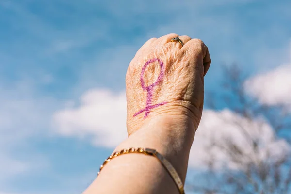 紫色の塗装爪を持つ高齢女性の拳 背景に空と 女性のシンボルが描かれています 女性の日 エンパワーメント 不平等 行動主義と抗議の概念 — ストック写真