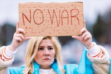 Ukraynalı sarışın ve ciddi jestli bir kadın, mavi ve sarı bir Ukrayna bayrağıyla sokakta Ukrayna-Rusya Savaşı 'nı protesto ediyor..