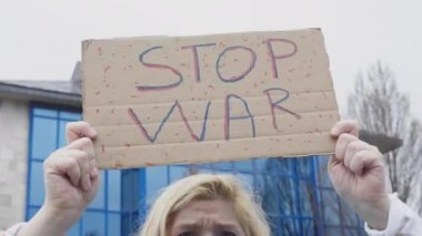 Ukraynalı sarışın ve ciddi jestli bir kadın, mavi ve sarı bir Ukrayna bayrağıyla sokakta Ukrayna-Rusya savaşını protesto eden 