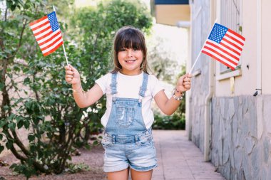 Evinin bahçesinde Amerikan bayrakları olan siyah saçlı küçük bir kız. Kutlama konsepti, bağımsızlık günü, 4 Temmuz, vatanseverlik, tatil ve Amerikan gururu..