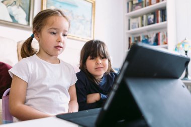 İki küçük kız dikkatle oturma odalarındaki tablette bir video izliyorlar. Çocukluk kavramı, teknoloji, öğrenme, eğlenme, internet ve bağlantı.