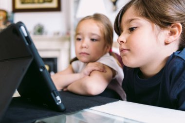 İki küçük kız dikkatle oturma odalarındaki tablette bir video izliyorlar. Çocukluk kavramı, teknoloji, öğrenme, eğlenme, internet ve bağlantı.
