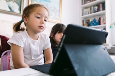 İki küçük kız dikkatle oturma odalarındaki tablette bir video izliyorlar. Çocukluk kavramı, teknoloji, öğrenme, eğlenme, internet ve bağlantı.