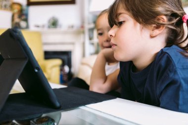 İki küçük kız dikkatle oturma odalarındaki tablette bir video izliyorlar. Çocukluk kavramı, teknoloji, öğrenme, eğlenme, internet ve bağlantı.