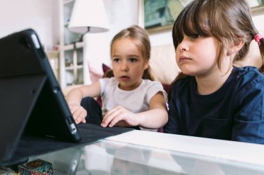 İki küçük kız dikkatle oturma odalarındaki tablette bir video izliyorlar. Çocukluk kavramı, teknoloji, öğrenme, eğlenme, internet ve bağlantı.